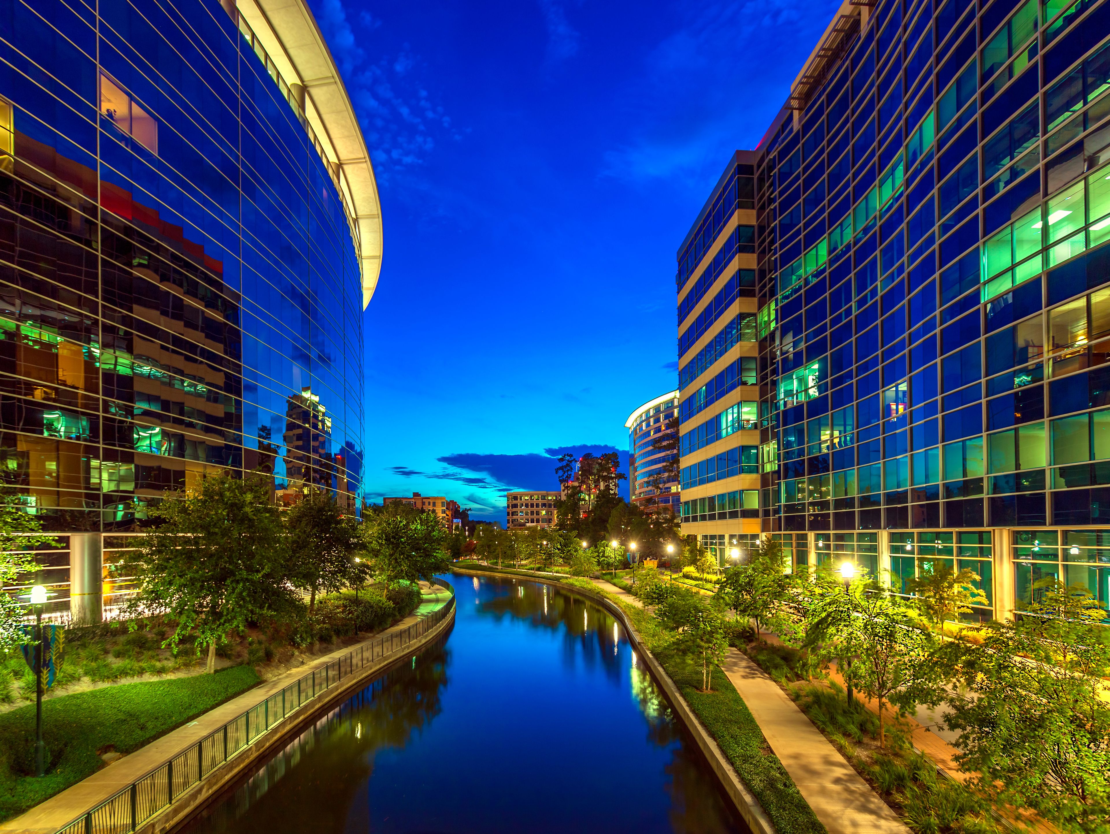 Paisagem urbana noturna com edifícios modernos, um rio e áreas verdes bem cuidadas.