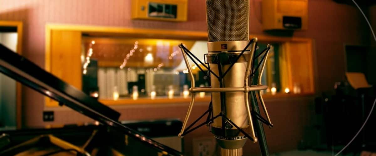 A microphone in a recording studio with a piano in the background.