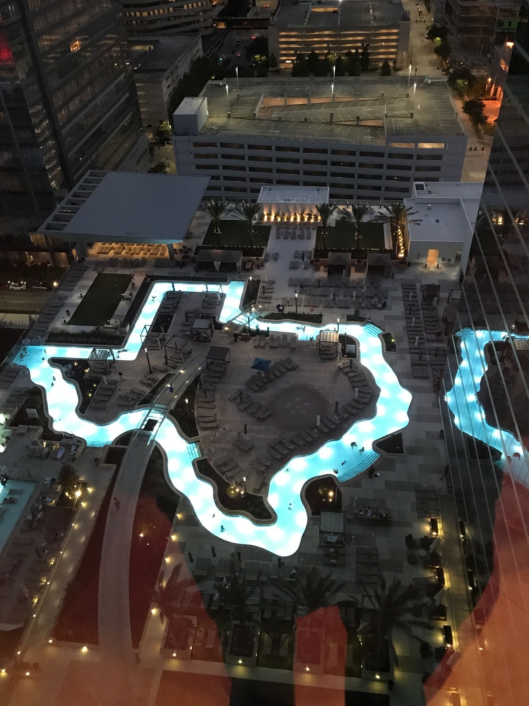 Vista aérea de una zona urbana moderna con una piscina distintiva con forma de corazón, rodeada de edificios y palmeras.