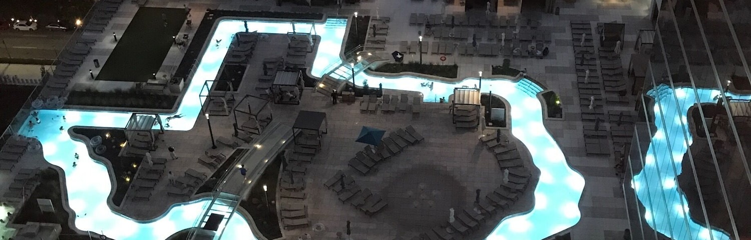 Vista aérea de una zona urbana moderna con una piscina distintiva con forma de corazón, rodeada de edificios y palmeras.
