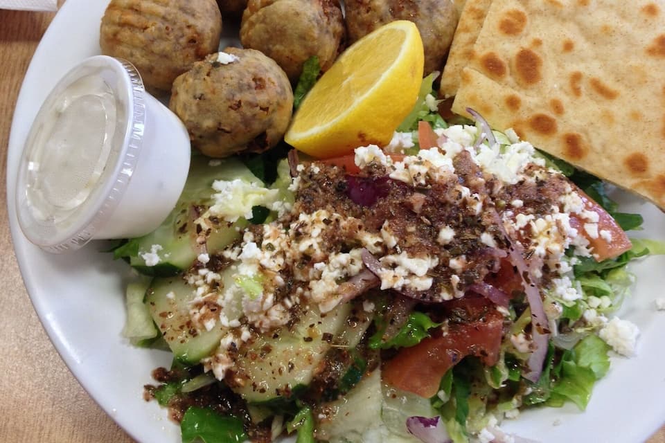 A plate of food with meatballs, fries, pita bread, and a salad with feta cheese.