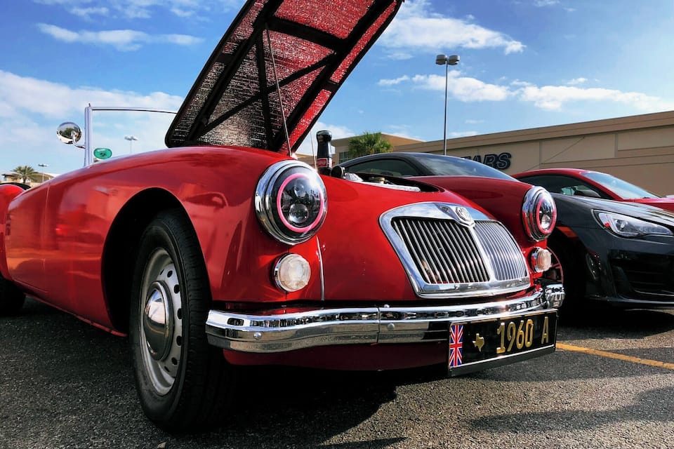 A classic red car with its hood open, parked in a lot.