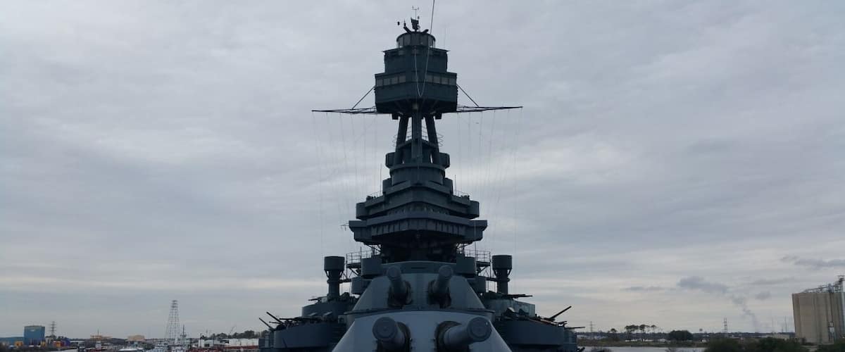 Een groot marineschip ligt aangemeerd in een haven met een heldere lucht.