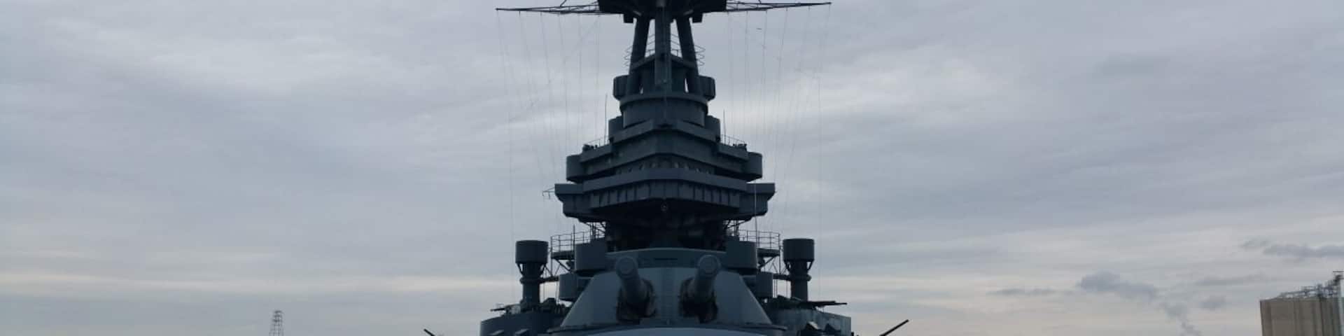 A large naval ship docked at a port with a clear sky.
