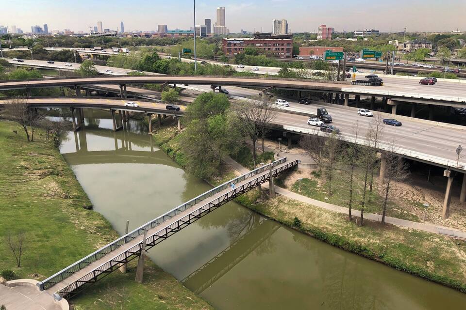 Un río cruzado por un puente, varias autopistas y edificios de la ciudad al fondo.