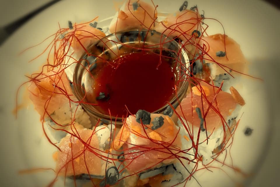 A plate of sushi with a red dipping sauce and thinly sliced fish.
