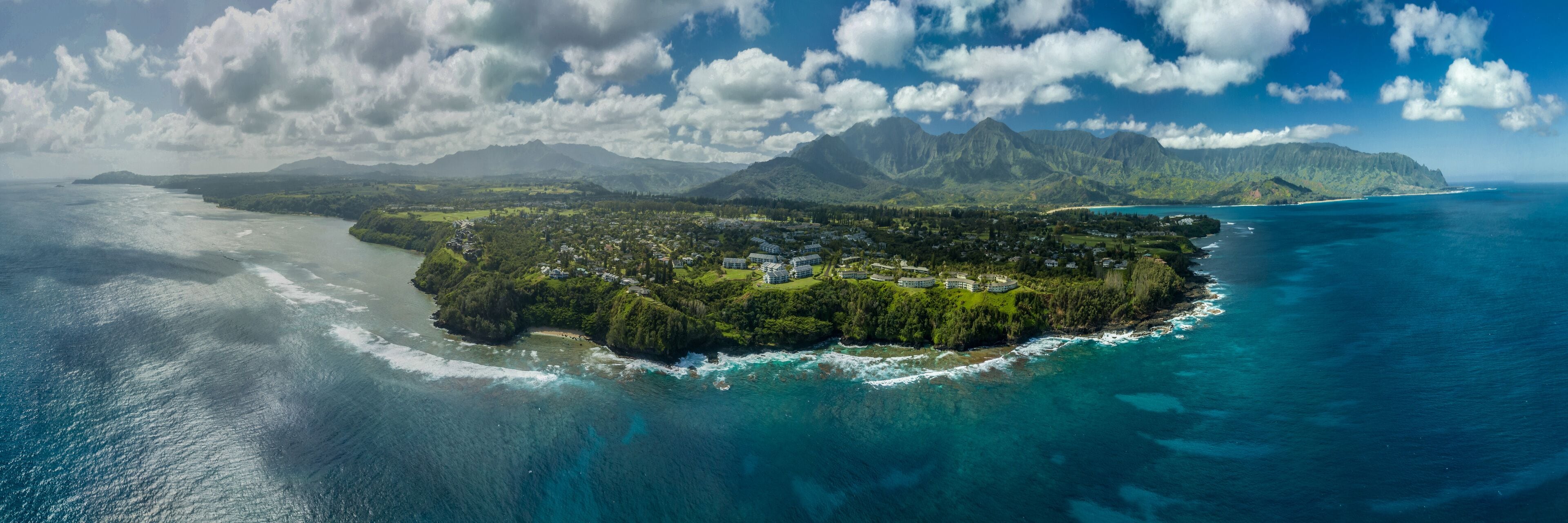 An aerial view of a lush, green island surrounded by turquoise waters, with a mountainous backdrop.