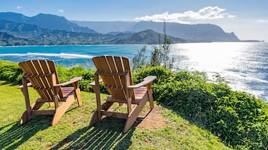 Two wooden Adirondack chairs overlooking a coastal landscape with mountains in the distance.