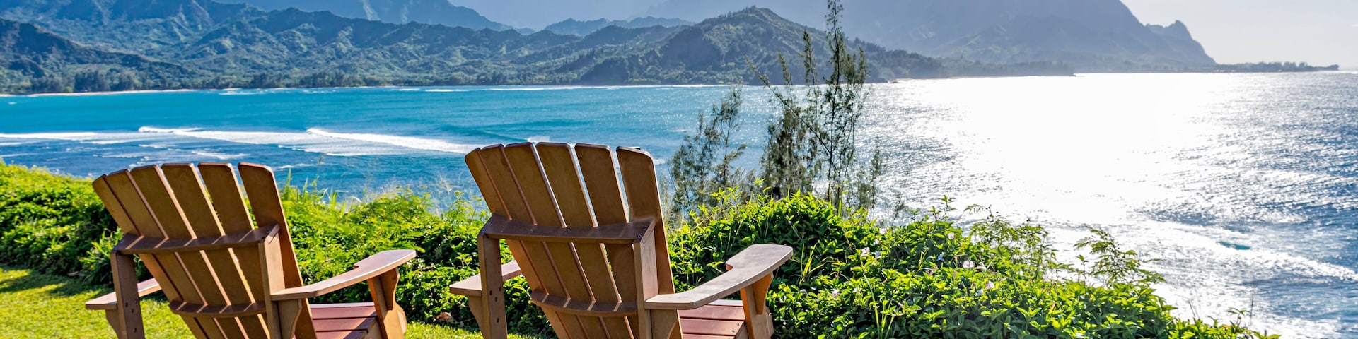 Two wooden Adirondack chairs overlooking a coastal landscape with mountains in the distance.