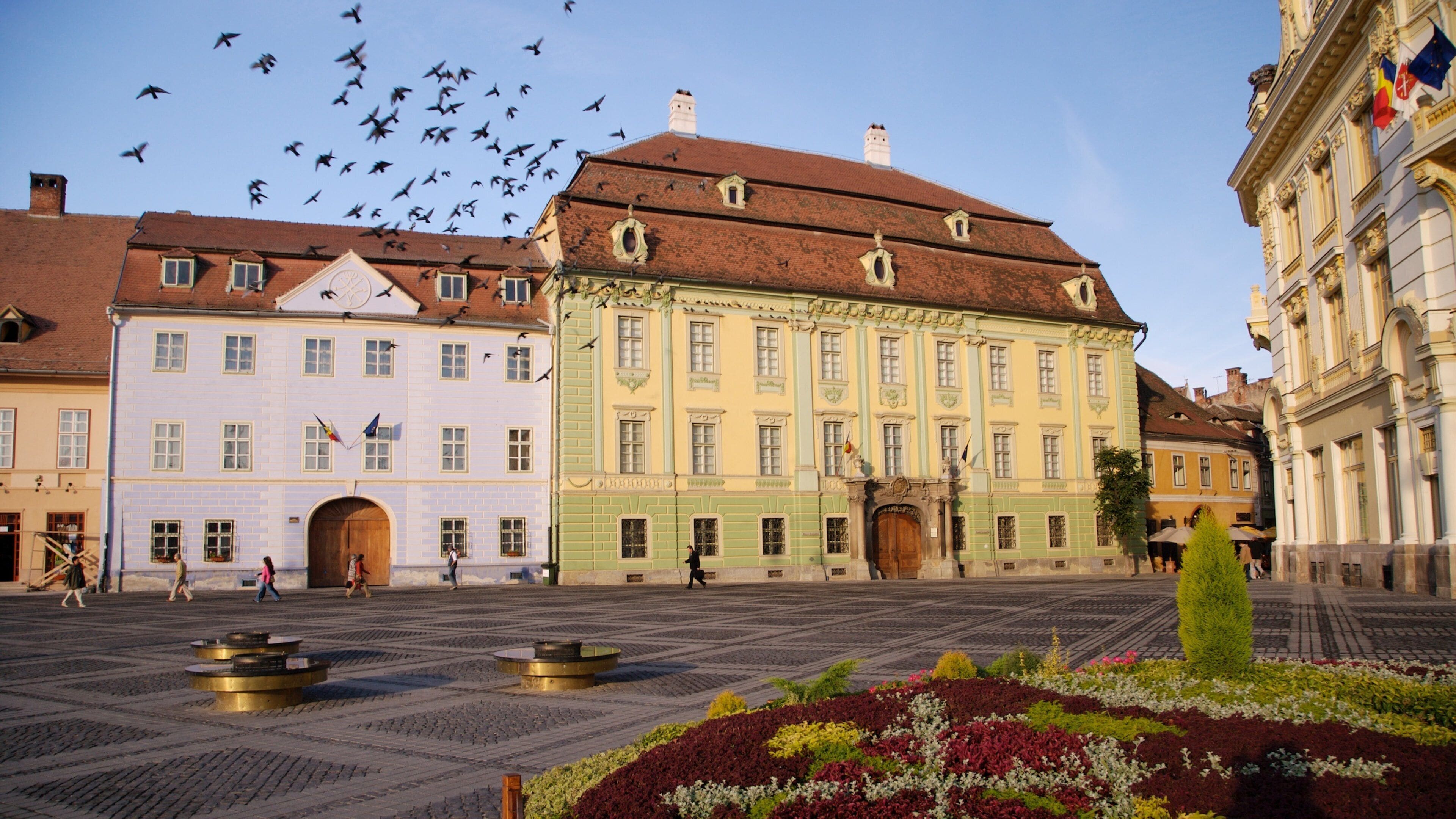A historic square with colorful buildings, a fountain, and a statue.