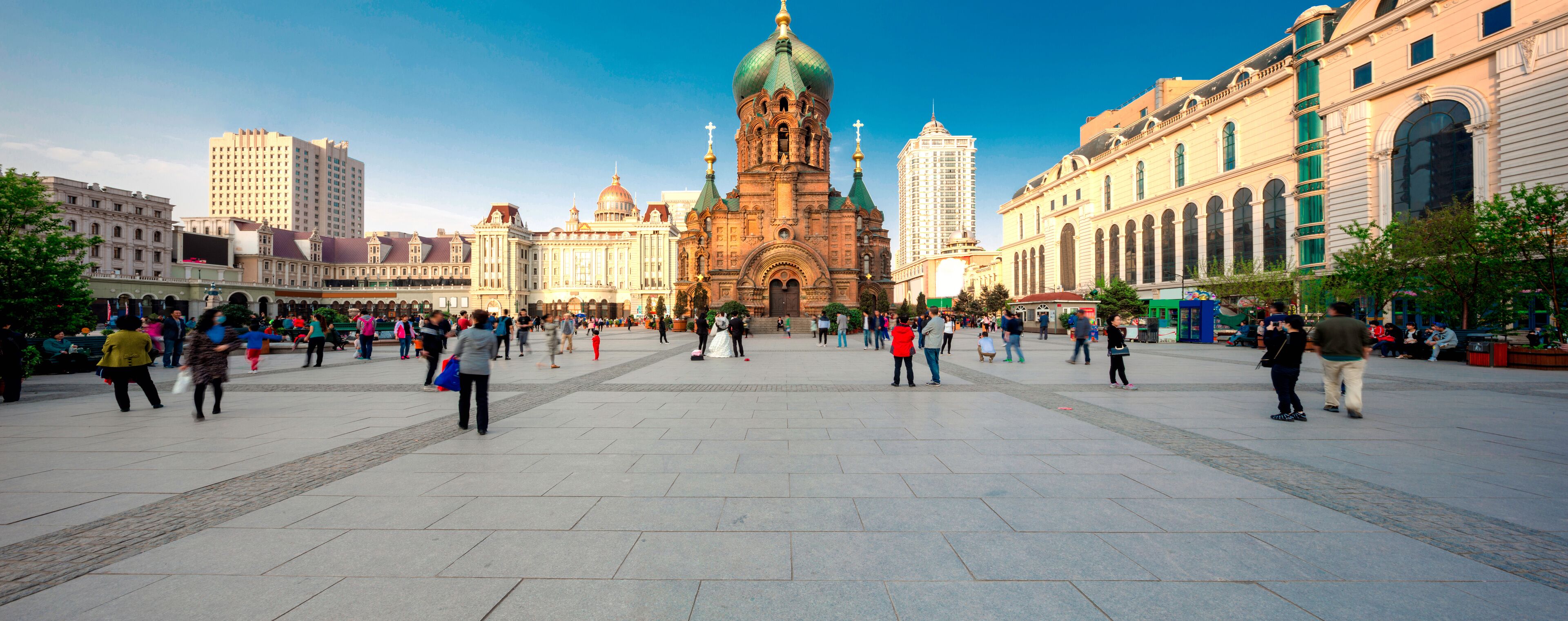 A large open square with a historic church in the center, surrounded by modern buildings.