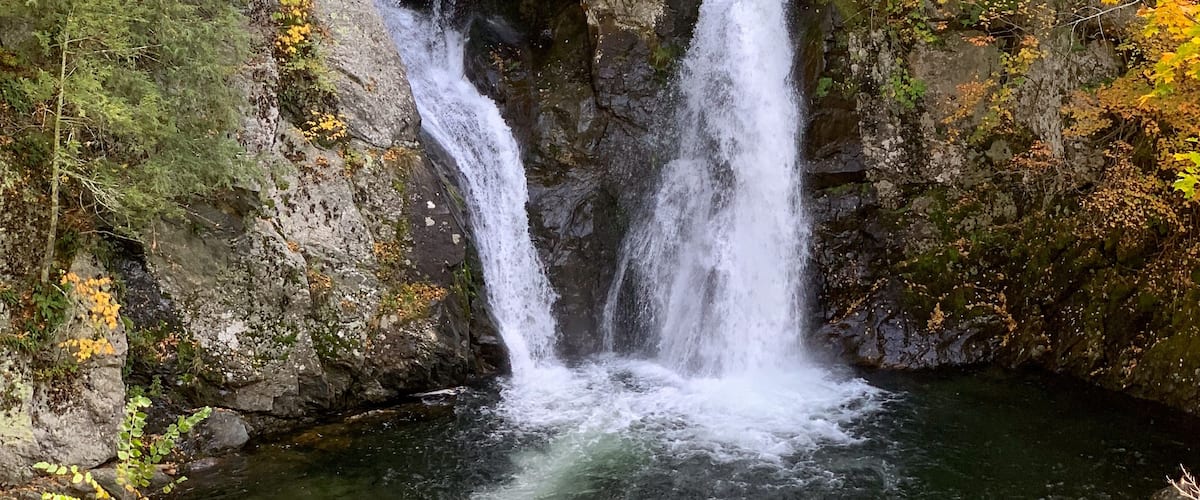 Bash Bish Falls cascades between granite cliffs amid vibrant autumn foliage in the Taconic Mountains, creating a scenic New England waterfall landscape.
