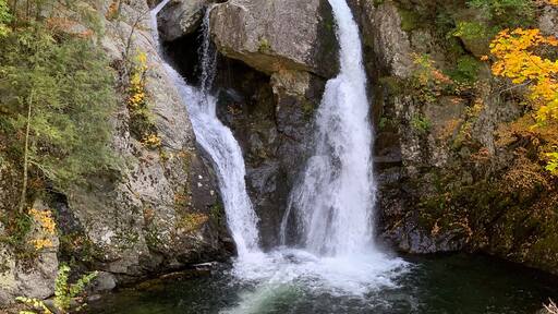 Bash Bish Falls cascades between granite cliffs amid vibrant autumn foliage in the Taconic Mountains, creating a scenic New England waterfall landscape.