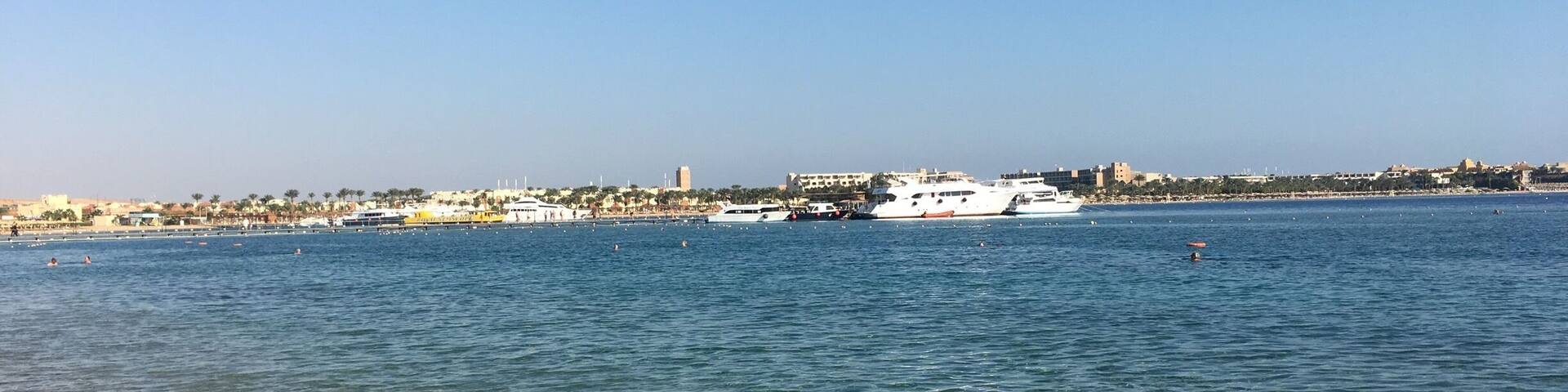 Un paysage urbain le long de la côte, avec un ciel bleu dégagé, une mer calme et plusieurs bateaux.