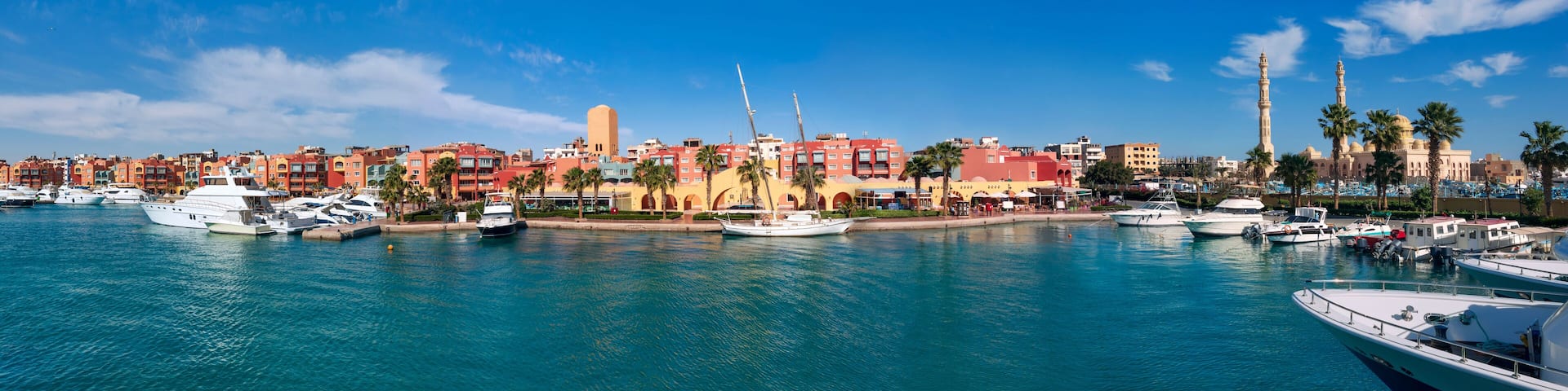 Panoramic view from the marina of Hurghada to the minarets of the El Mina mosque and the city's embankment with moored yachts, shops, cafes and a pedestrian zone for walking