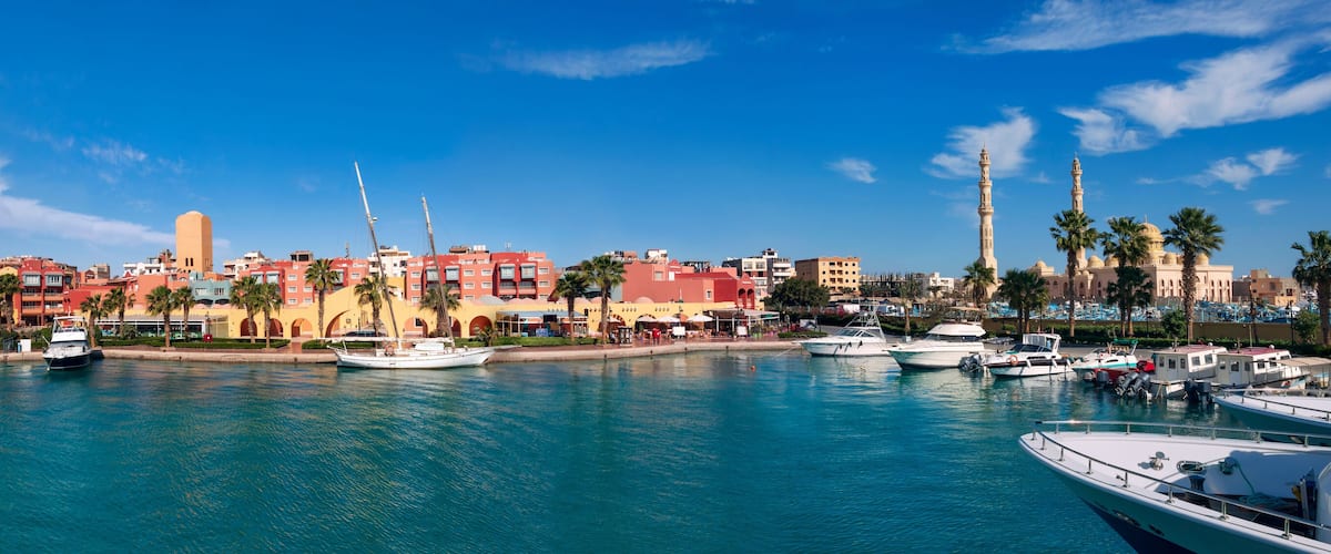 A marina with boats, a mosque with minarets, and colorful buildings along the waterfront.