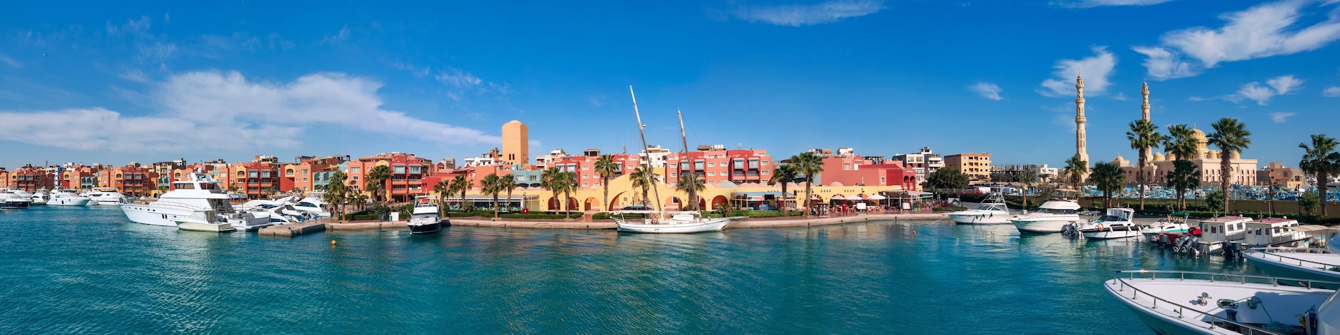 A marina with boats, a mosque with minarets, and colorful buildings along the waterfront.