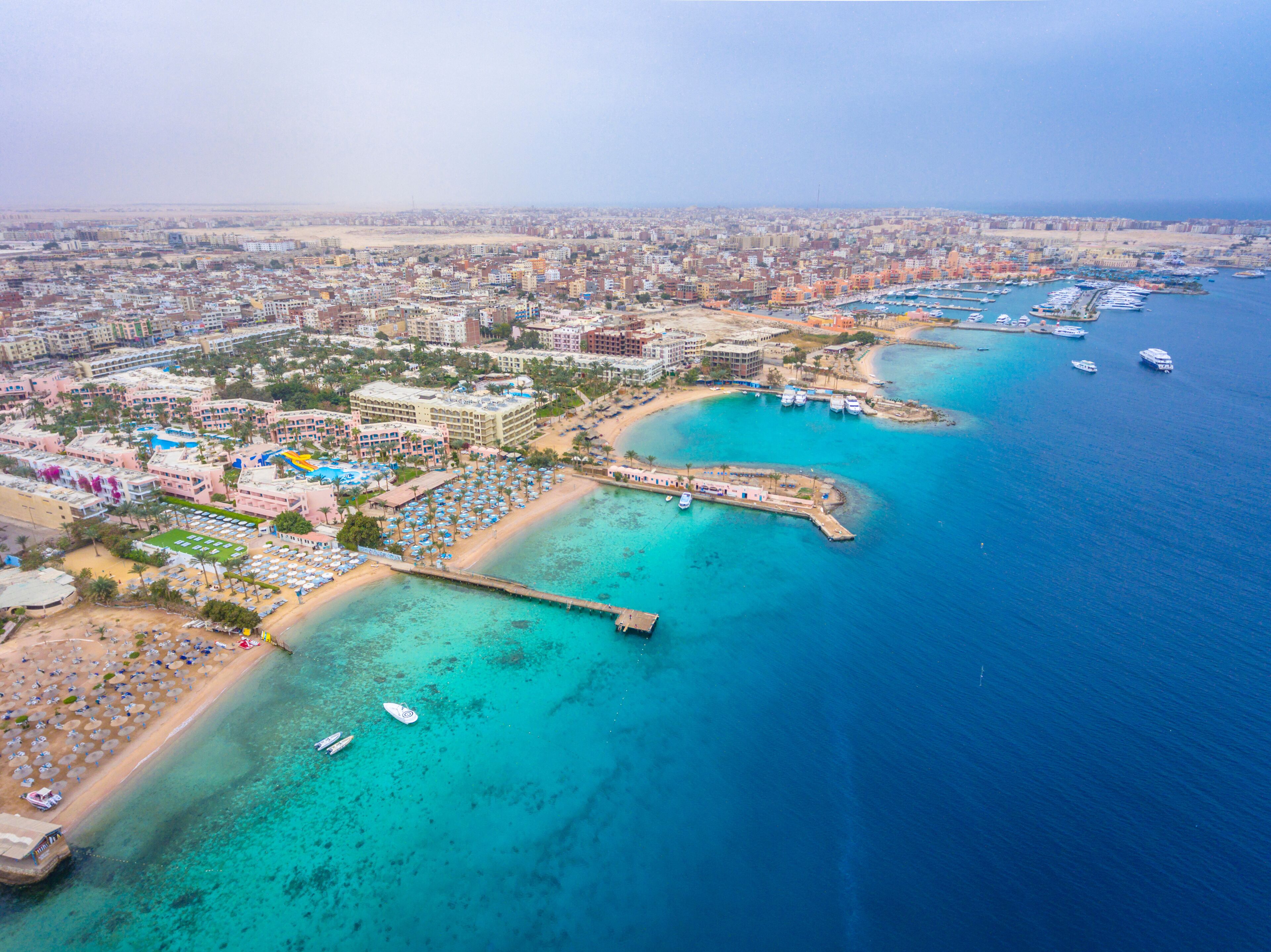 Vista aérea de una ciudad costera con puerto deportivo, playa y área urbana densa.