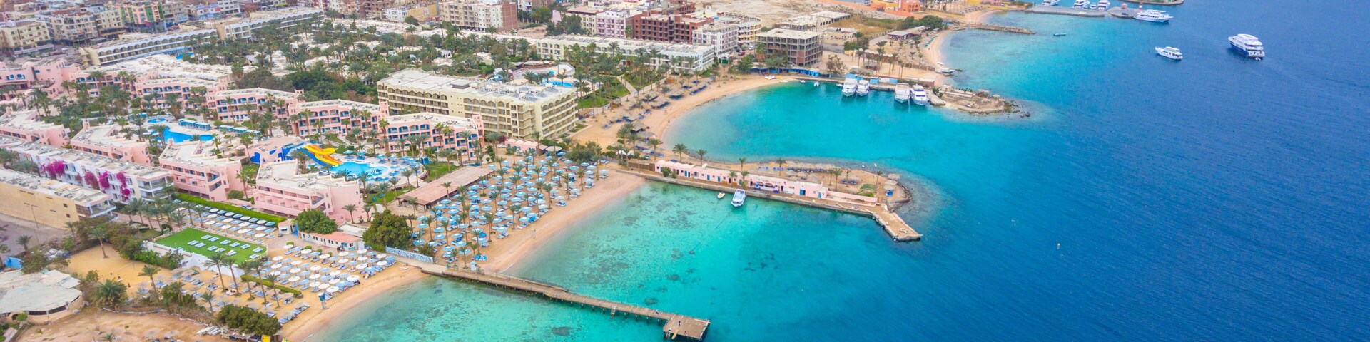 Vista aérea de una ciudad costera con puerto deportivo, playa y área urbana densa.