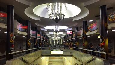 Un espacio interior moderno con una escalera central, grandes candelabros y anuncios de Nescafe Gold.