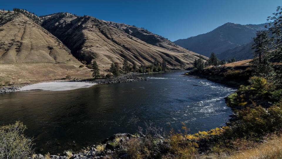 A river flowing through a mountainous landscape with rocky banks and sparse vegetation.