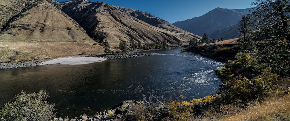 A river flowing through a mountainous landscape with rocky banks and sparse vegetation.