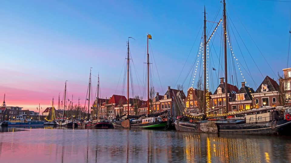 A harbor at dusk with boats docked, buildings with red roofs, and a clear sky.