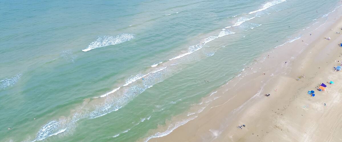 An aerial view of a beach with gentle waves, a sandy shore, and scattered beachgoers.