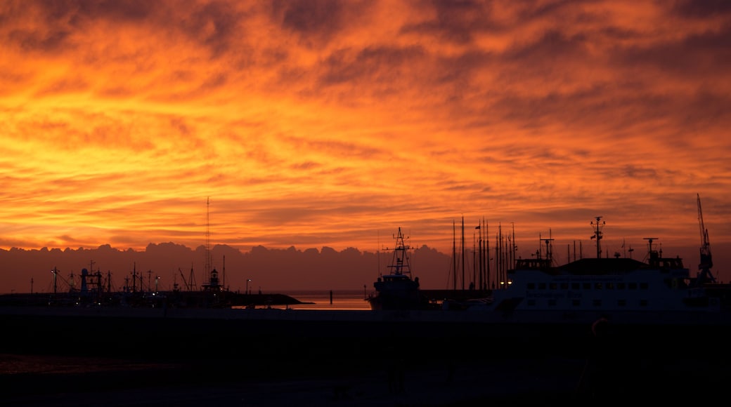 Un atardecer sobre un puerto con barcos y estructuras industriales silueteadas contra el cielo.