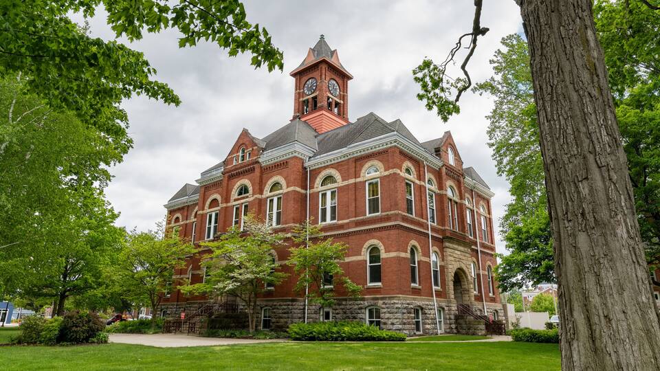 A large brick building with a clock tower, surrounded by green grass and trees.