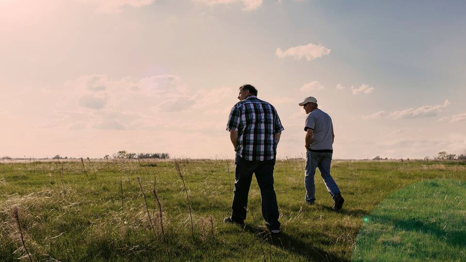 Two people walking in a grassy field with a clear sky.