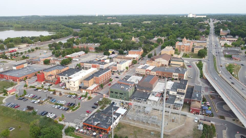 An aerial view of a town with a mix of historic and modern buildings, a large body of water in the background, and a highway running through the center.