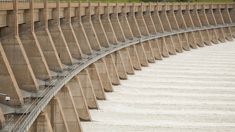 A large dam with a walkway and a river flowing through it.