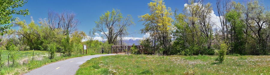 Jordan River Parkway Trail, Redwood Trailhead bordering the Legacy Parkway Trail, panorama views with surrounding trees and silt filled muddy water along the Rocky Mountains, Salt Lake City, Utah.