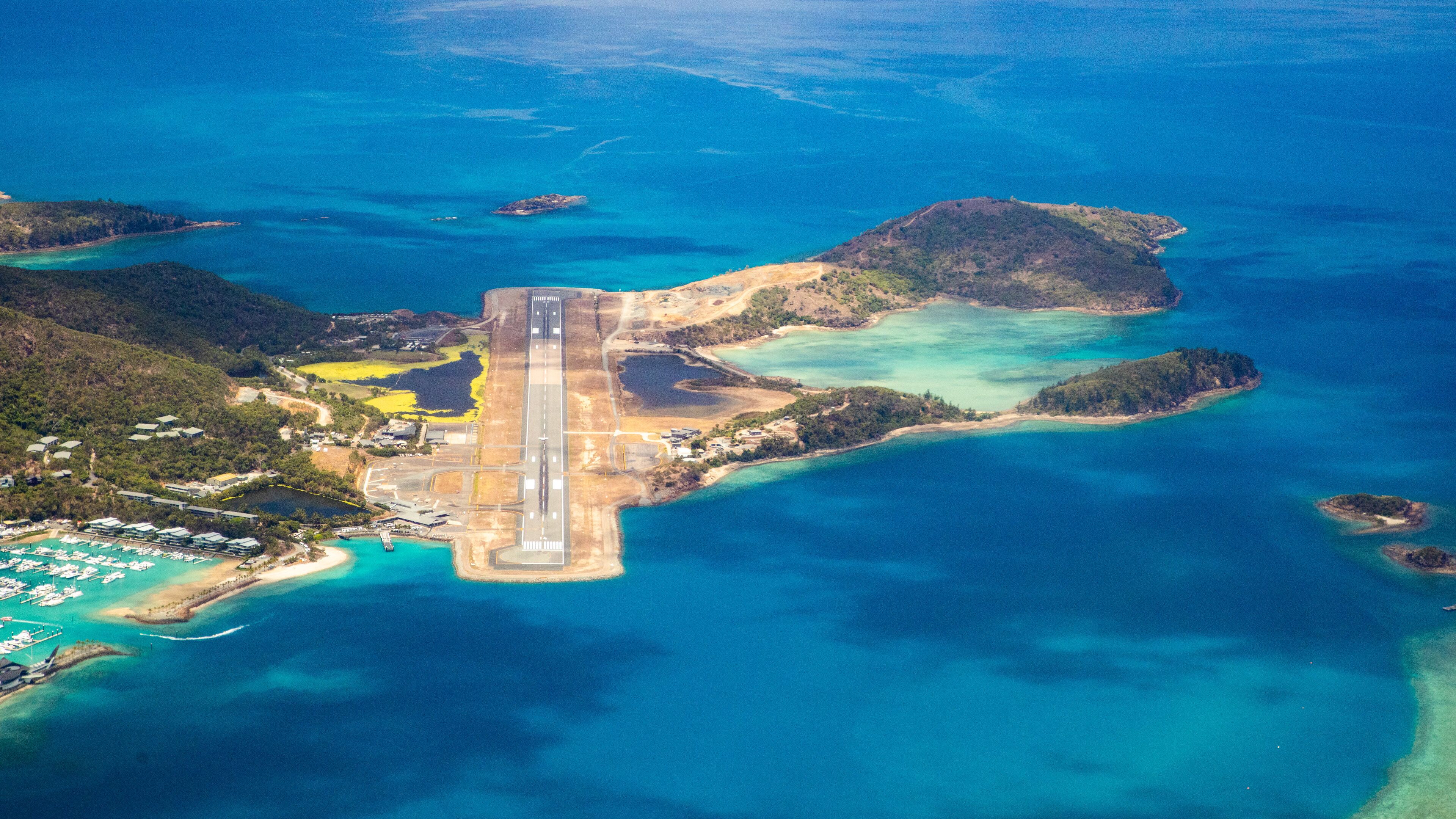 An aerial view of a coastal area with a runway, clear blue waters, and surrounding islands.