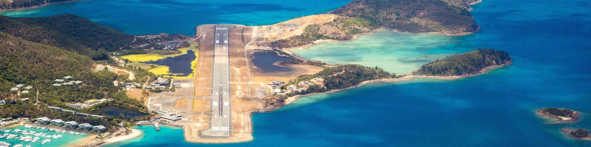 Vista aérea de una zona costera con una pista de aterrizaje, aguas azules cristalinas e islas circundantes.