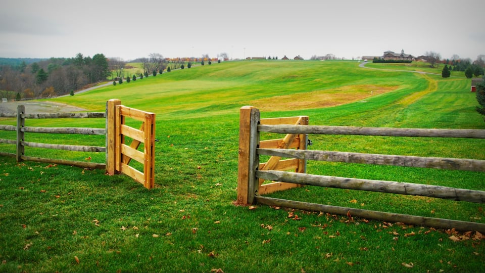 A wooden gate in a grassy field with a hilly landscape in the background.
