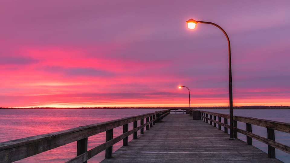 A wooden pier extending into a body of water with a sunset sky.