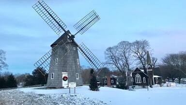 A windmill with a closed sign, surrounded by snow-covered ground and bare trees.