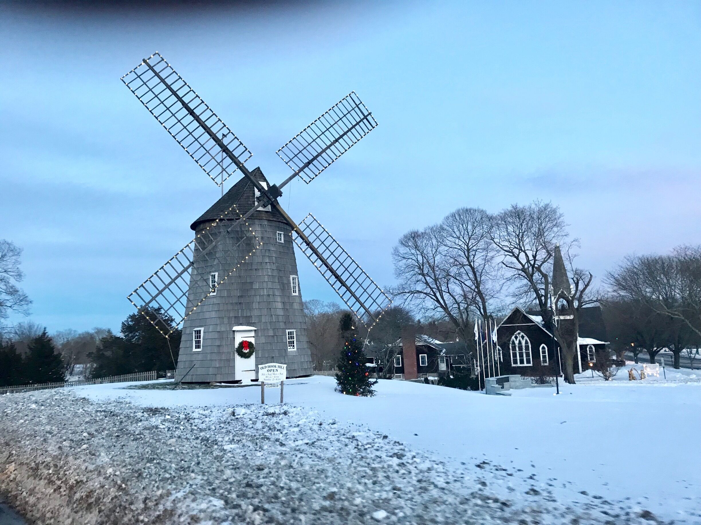 A windmill with a closed sign, surrounded by snow-covered ground and bare trees.