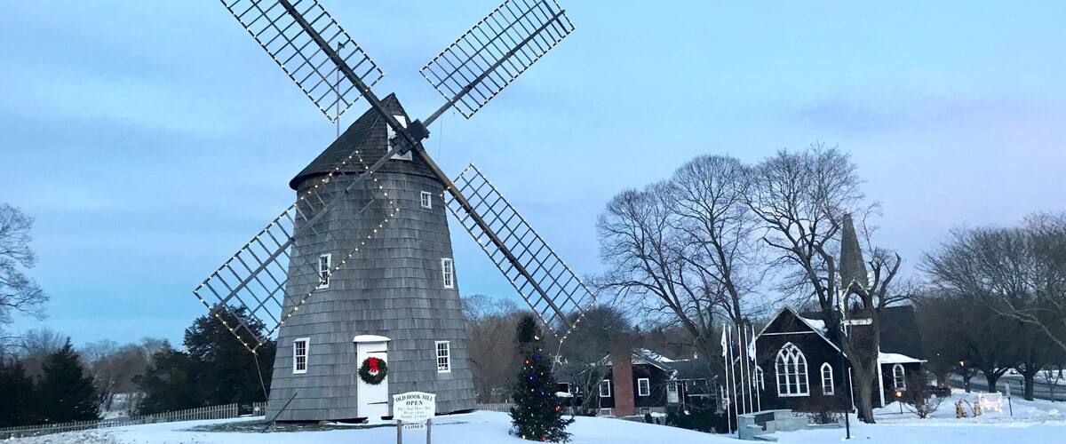 A windmill with a closed sign, surrounded by snow-covered ground and bare trees.