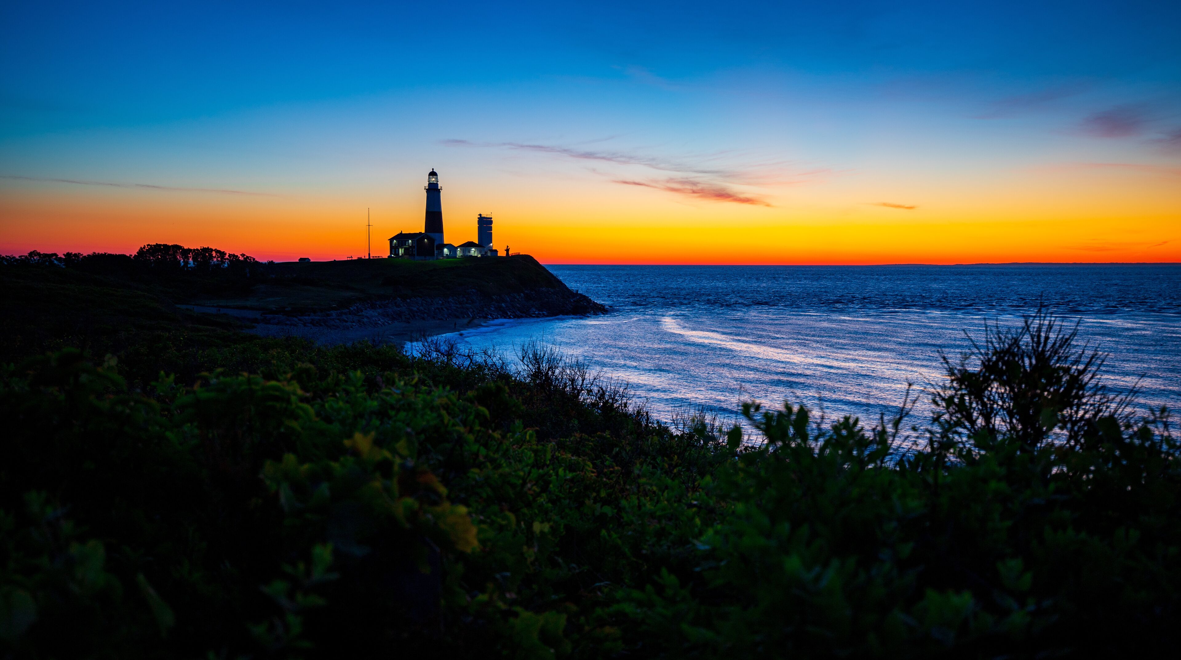 A lighthouse at sunset with a clear sky and ocean.