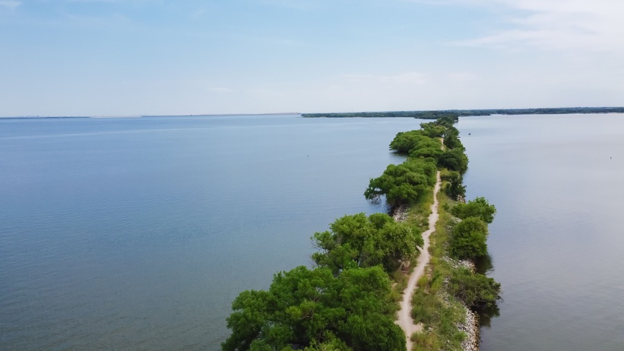 Aerial view lakeside long straight hiking trail with lush green tree lead to The Old Lake Dallas Dam from Lake Lewisville, Texas, America
