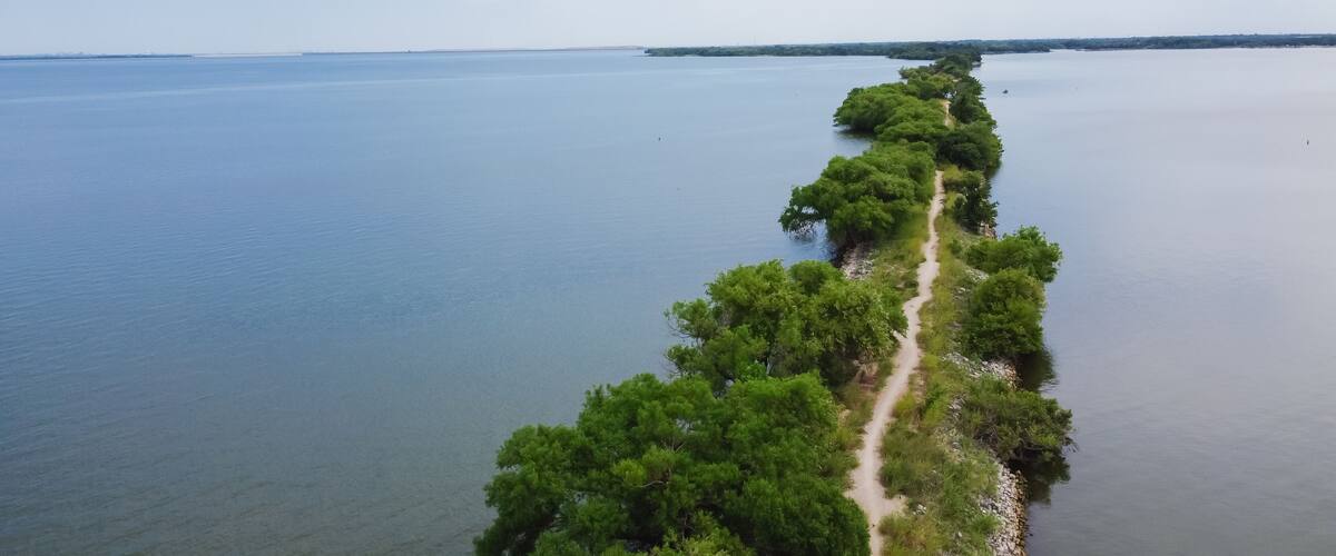 Aerial view lakeside long straight hiking trail with lush green tree lead to The Old Lake Dallas Dam from Lake Lewisville, Texas, America