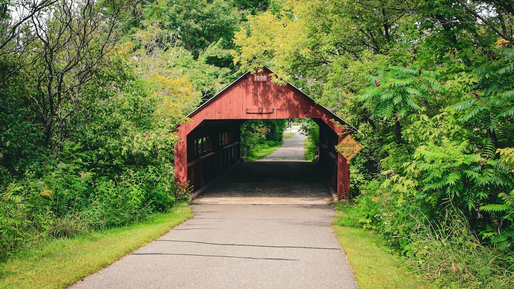 A red covered bridge with the year 1998 marked on it, surrounded by lush greenery.