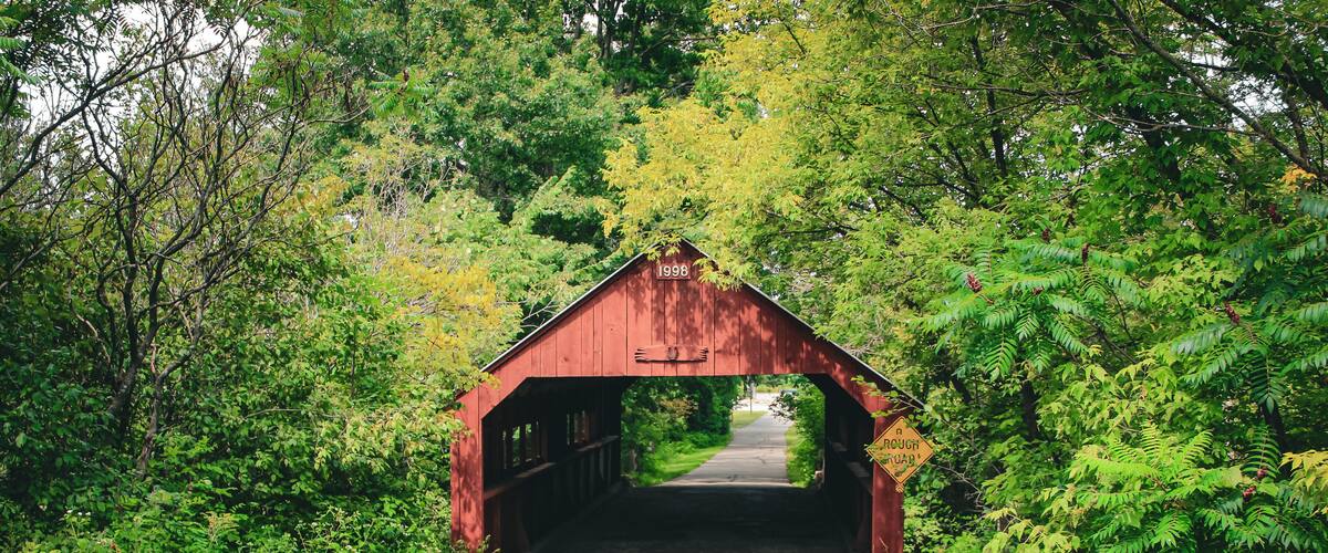 A red covered bridge with the year 1998 marked on it, surrounded by lush greenery.