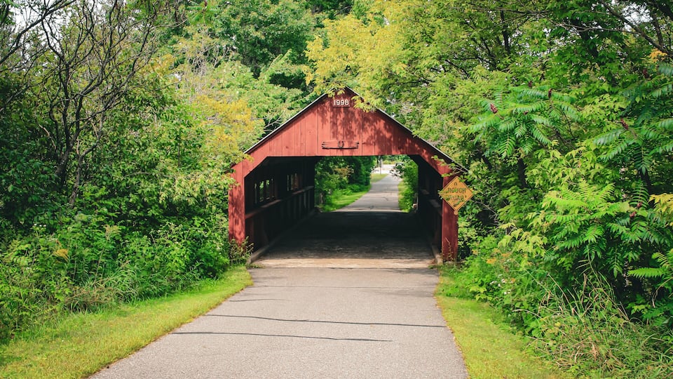 A red covered bridge with the year 1998 marked on it, surrounded by lush greenery.