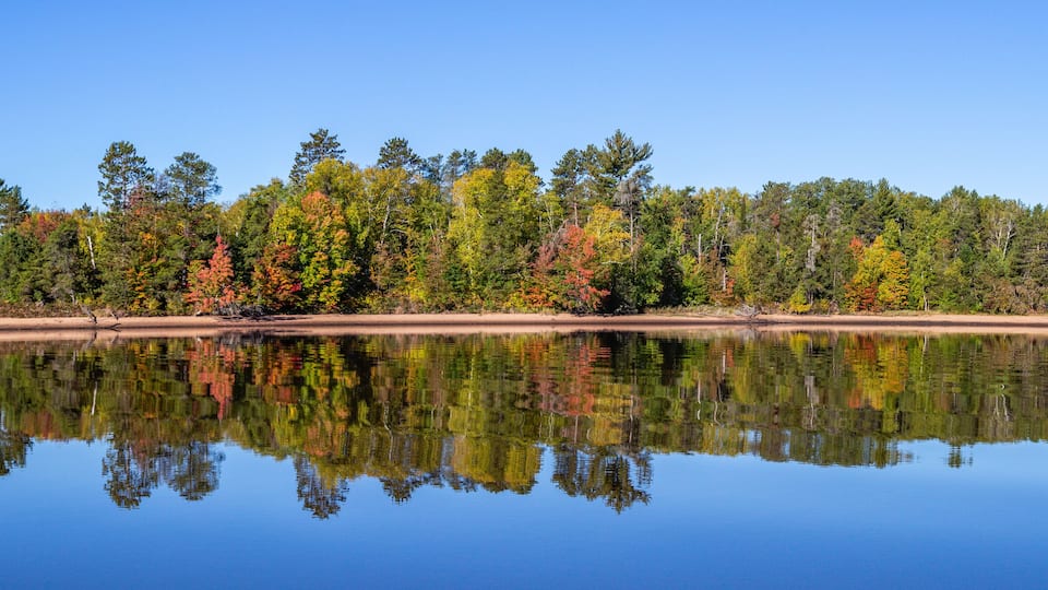A calm lake reflecting a forest of autumn-colored trees.