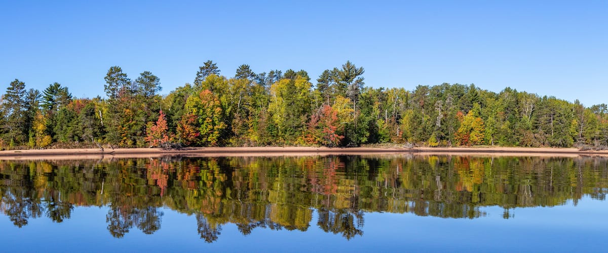 A calm lake reflecting a forest of autumn-colored trees.