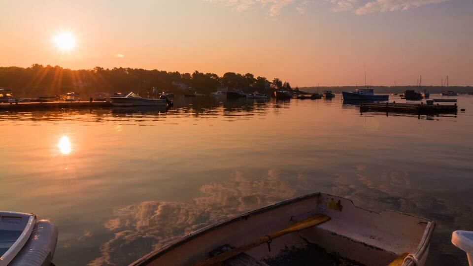 A calm harbor at sunset with boats docked, a wooden pier, and a clear sky.